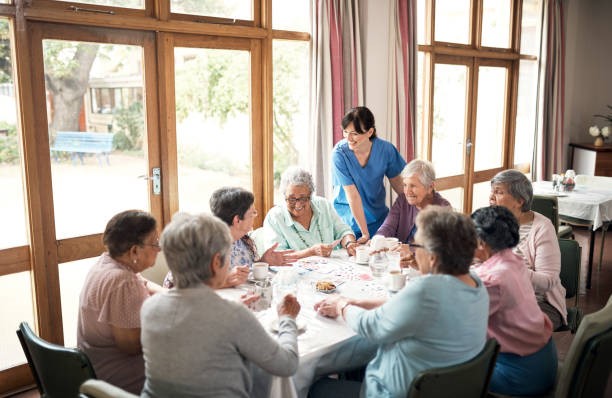 Visuel de personnes âgées prenant le thé autour d'une table interagissant avec une infirmière , évoquant une résidence pour femmes âgées
